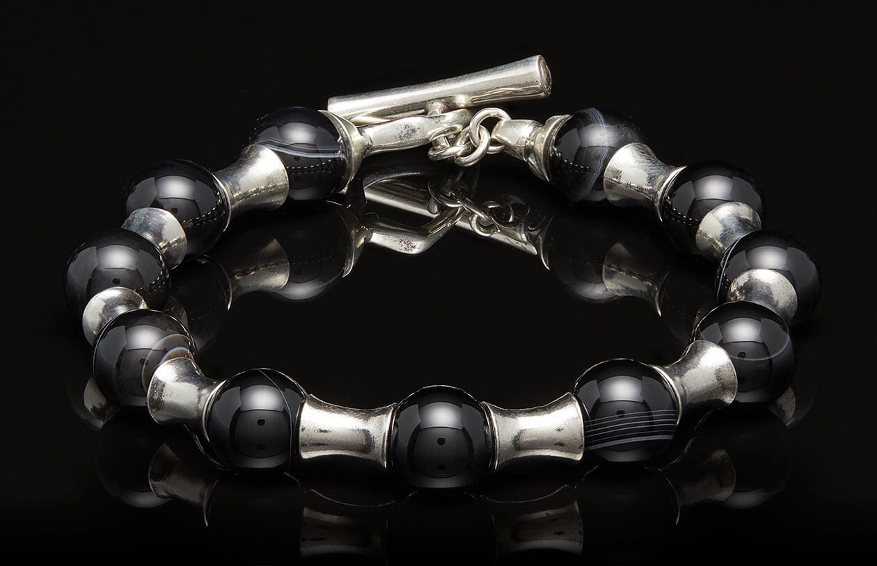 Black and silver beaded bracelet with a toggle clasp, displayed on a reflective black surface.