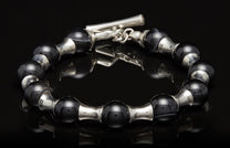 Black and silver beaded bracelet with a toggle clasp, displayed on a reflective black surface.