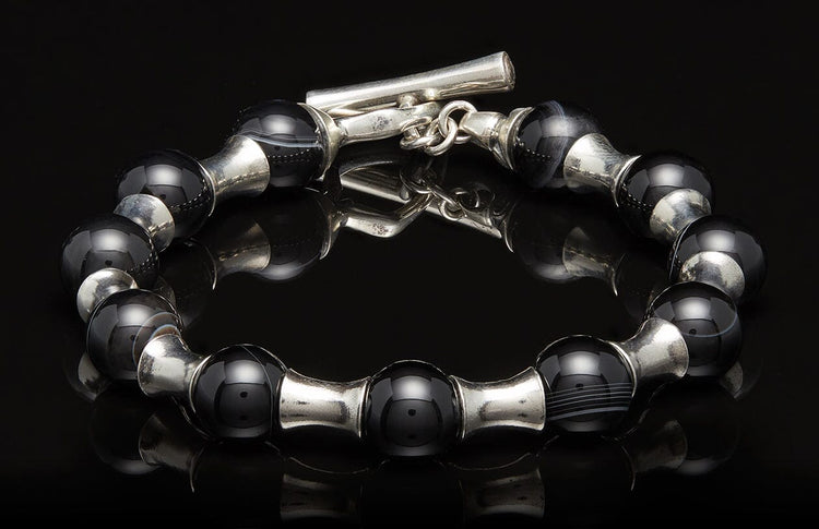Black and silver beaded bracelet with a toggle clasp, displayed on a reflective black surface.