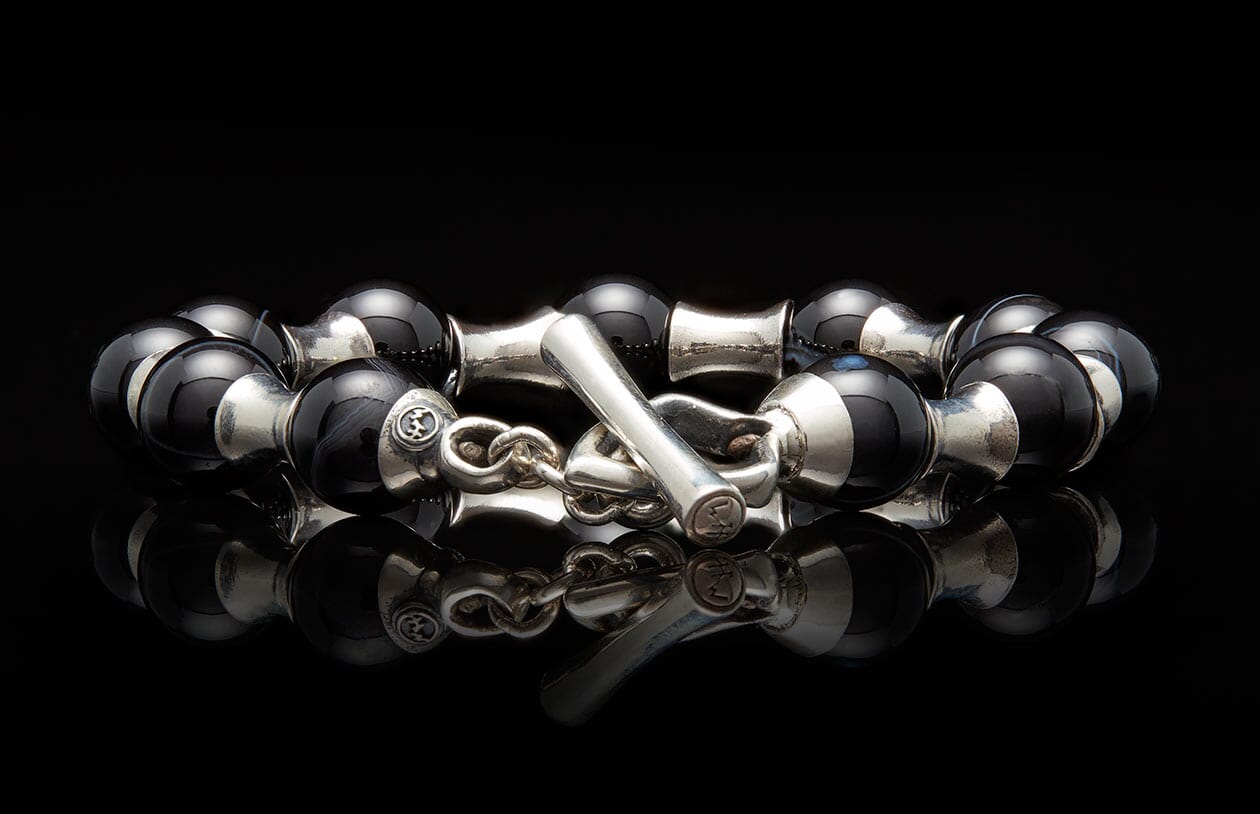 Black and silver beaded bracelet with a toggle clasp featuring engraved symbols, reflected on a dark surface.