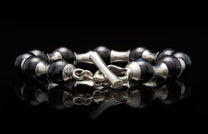 Black and silver beaded bracelet with a toggle clasp featuring engraved symbols, reflected on a dark surface.