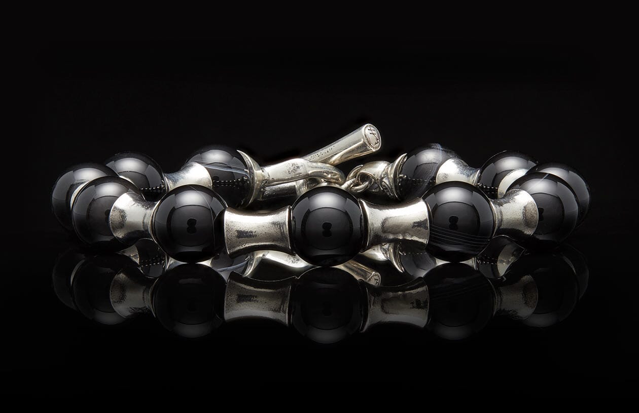 Black onyx and silver beaded bracelet with hourglass links and a cross-engraved toggle clasp.