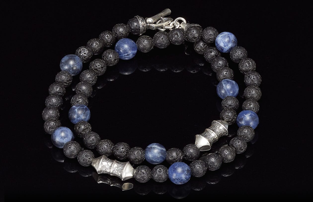 A coiled beaded necklace/bracelet with blue sodalite and black lava beads, featuring ornate silver spacers and clasp.