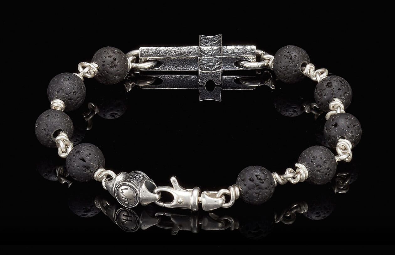 Black lava bead bracelet with silver links, a central hammered silver cross, and an engraved clasp.
