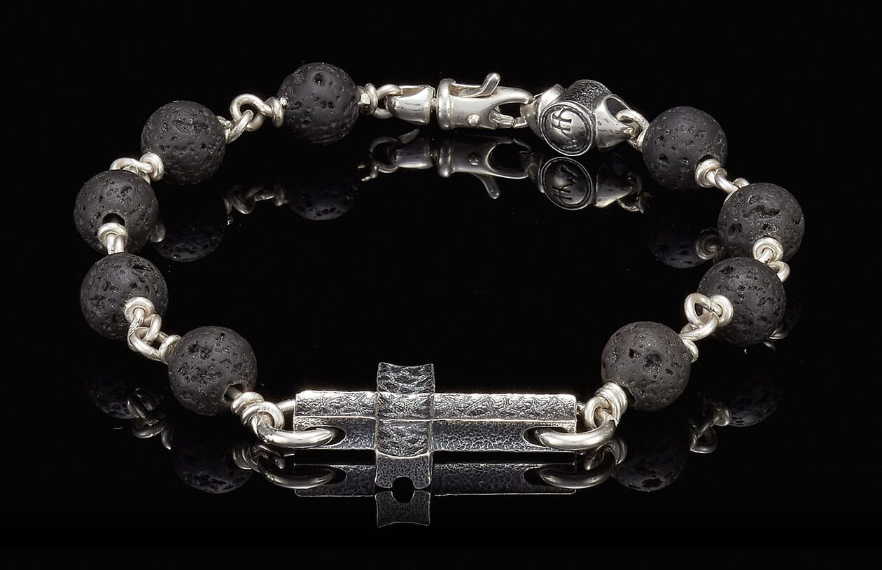 Black lava bead bracelet with silver links, a textured silver cross charm, and a silver lobster clasp.
