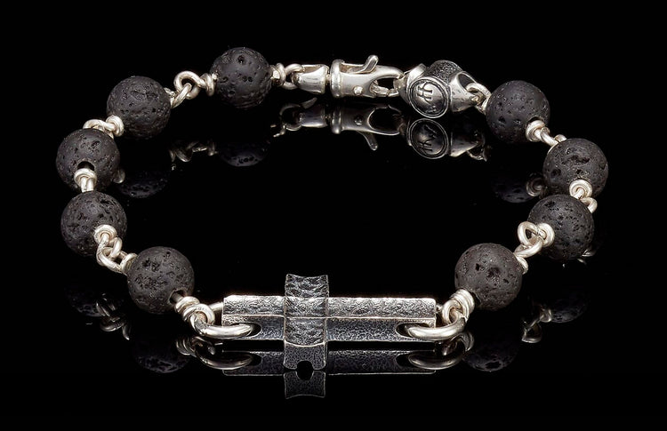 Black lava bead bracelet with silver links, a textured silver cross charm, and a silver lobster clasp.