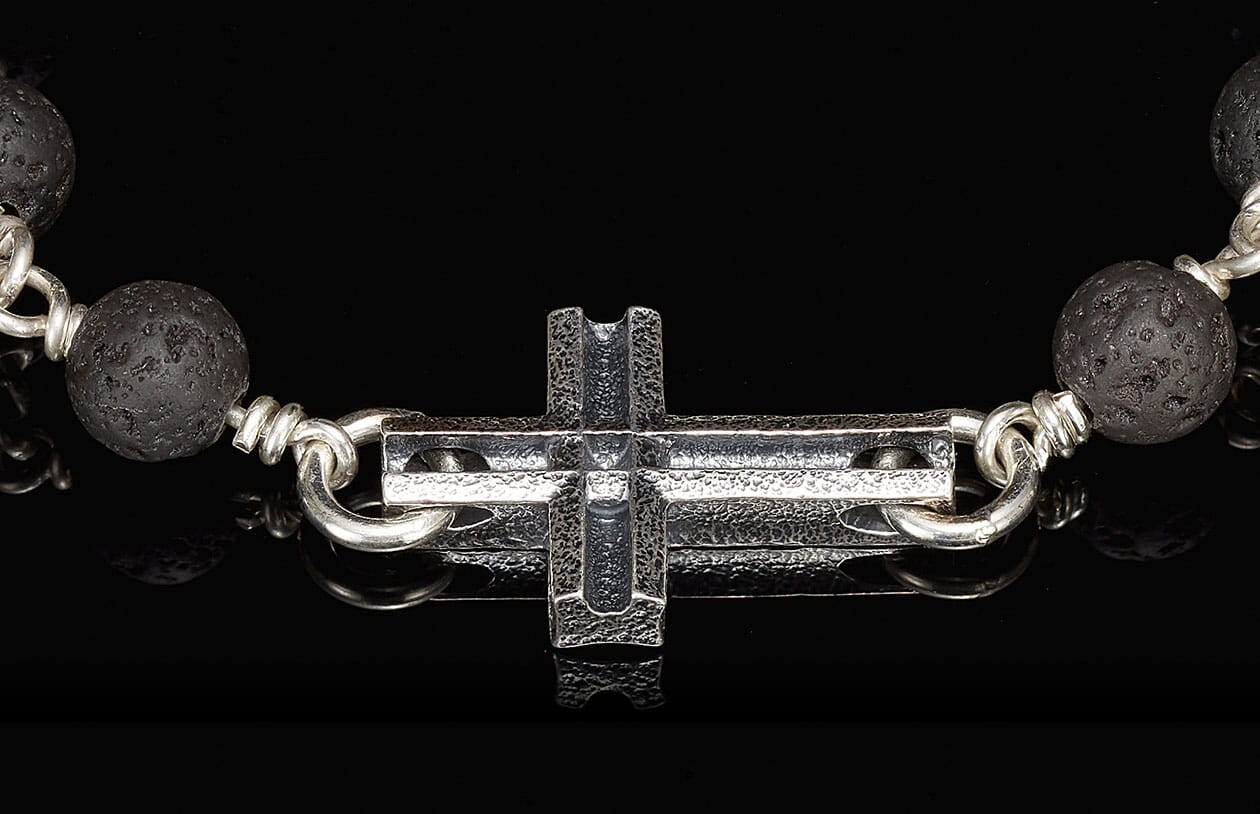 Black lava bead and textured silver cross bracelet with reflective black background.