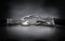 Silver jewelry clasp featuring elaborate decorative metalwork, connected to a black braided cord.