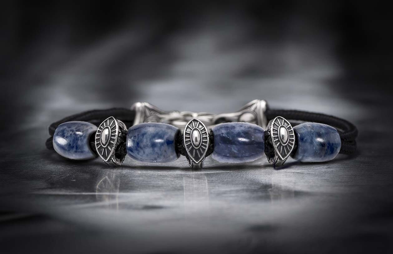 Sodalite bracelet with natural blue beads, intricate silver shield-like charms, and a dark braided cord.