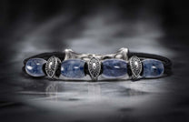 Sodalite bracelet with natural blue beads, intricate silver shield-like charms, and a dark braided cord.