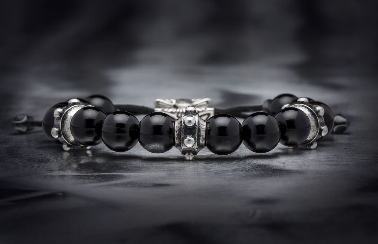 Black sardonyx beaded bracelet with intricate silver metal spacers, lying on a dark textured surface.