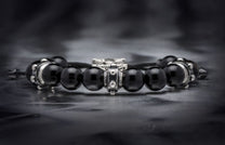 Black sardonyx beaded bracelet with intricate silver metal spacers, lying on a dark textured surface.
