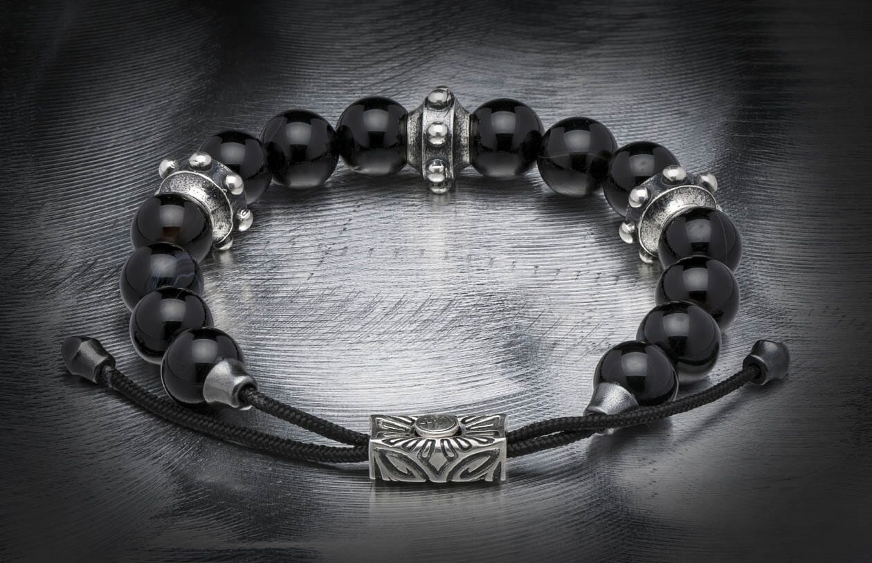 Black sardonyx beaded bracelet with silver-toned metal spacers and an adjustable cord, displayed on a brushed metallic surface.