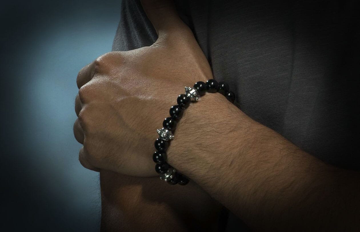 Black sardonyx beaded bracelet with silver barrel-shaped spacers, worn on a man's arm.