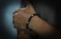Black sardonyx beaded bracelet with silver barrel-shaped spacers, worn on a man's arm.