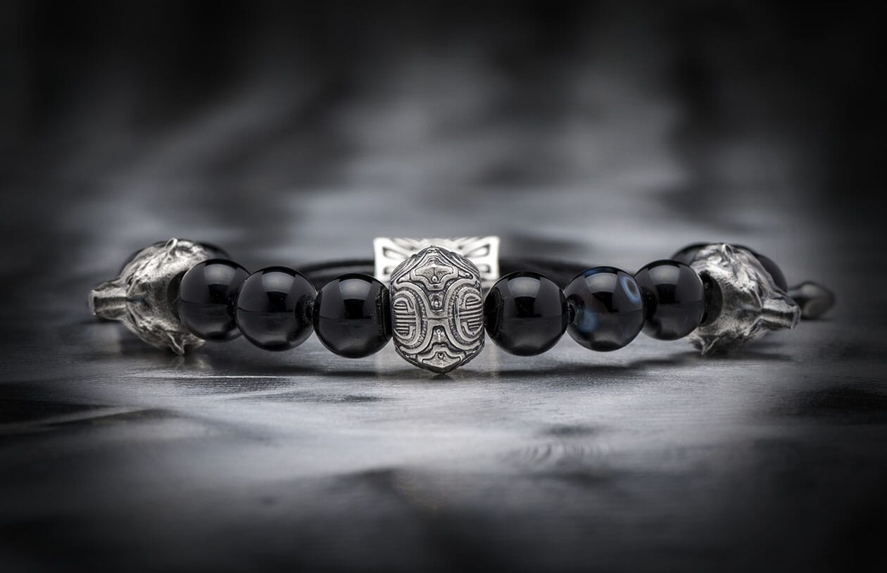 Black beaded bracelet with a central intricately patterned silver bead and silver wolf head terminals.