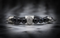 Black beaded bracelet with a central intricately patterned silver bead and silver wolf head terminals.