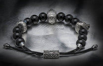 Black beaded bracelet with silver animal head beads, an ornate central bead, and a rectangular clasp on a brushed metal surface.