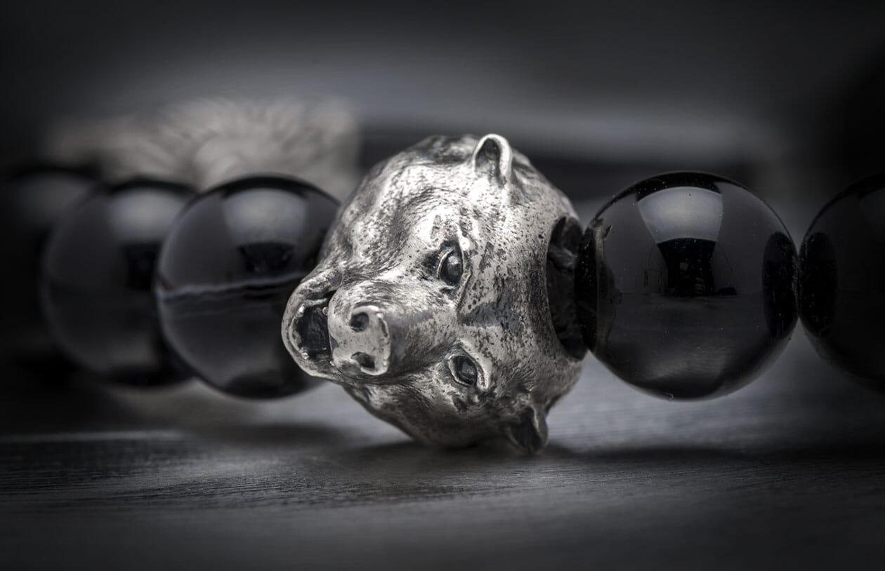 Black bead bracelet with a detailed, textured silver wild boar head charm on a dark surface.