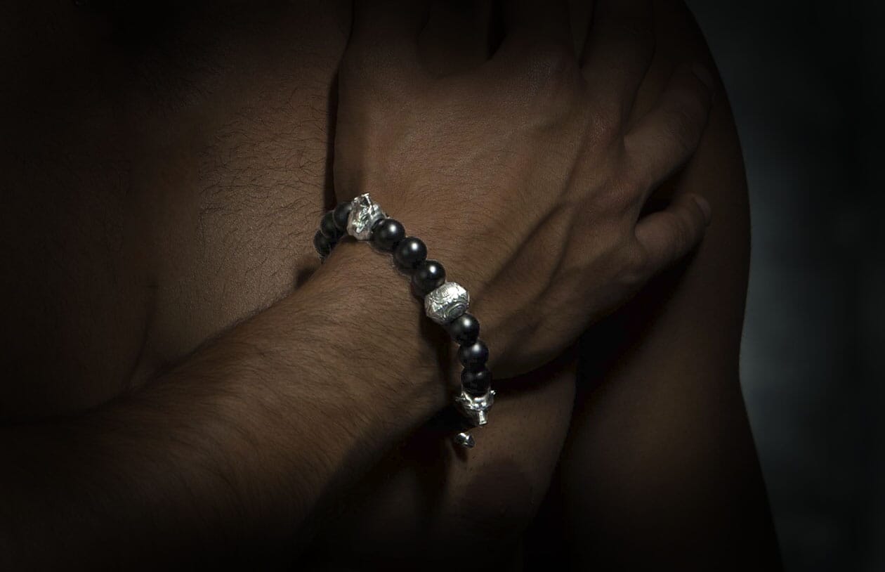 Black beaded bracelet featuring silver skull and intricate round beads on a man's arm.
