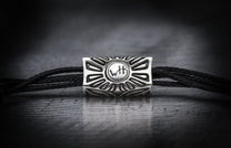 Black cord bracelet with a silver-toned metal bead featuring a carved sunburst design and central 'WtH' initials.