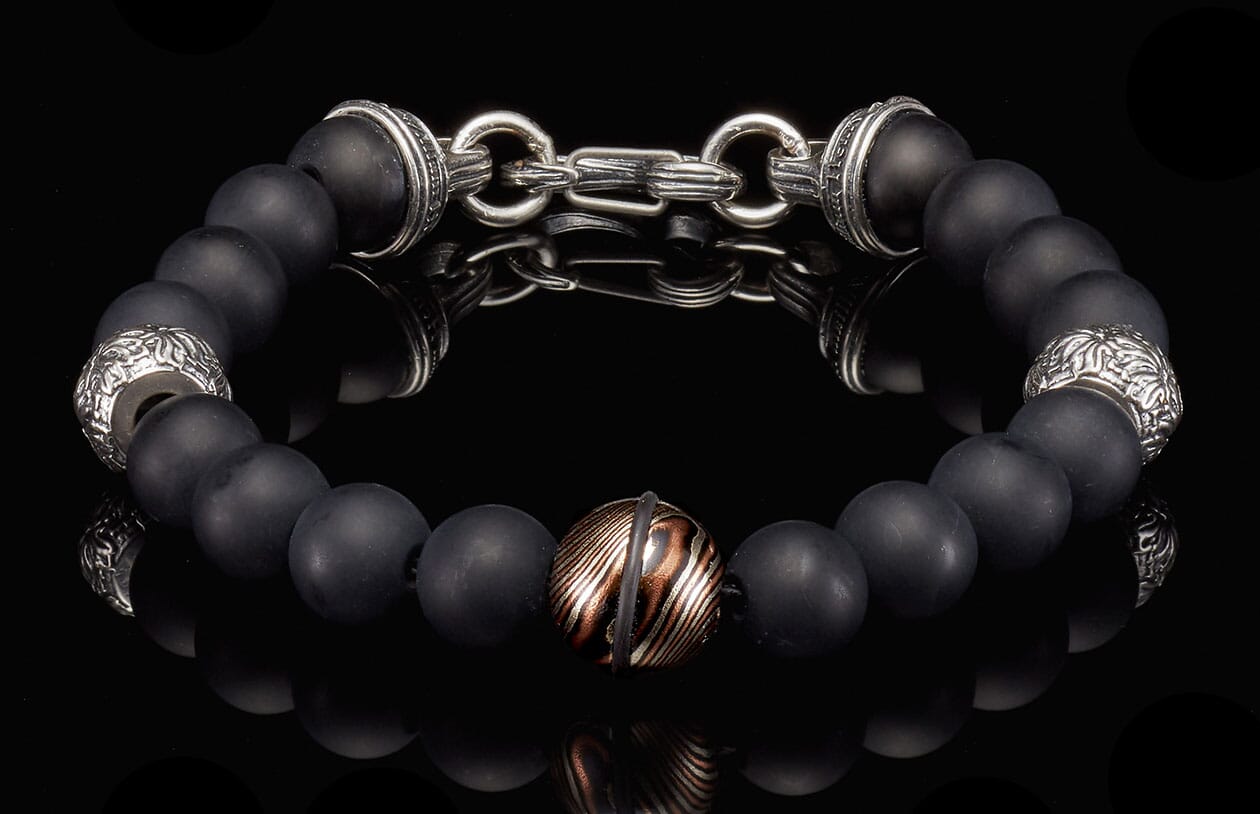 Black matte beaded bracelet with silver-tone decorative elements, a central copper-striped bead, and a silver chain clasp.