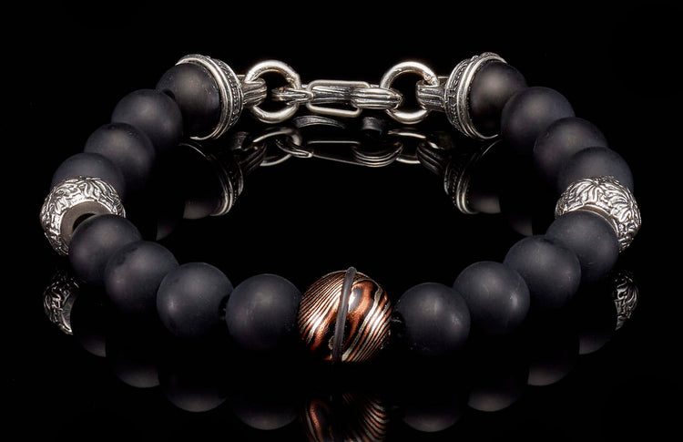 Black matte beaded bracelet with silver-tone decorative elements, a central copper-striped bead, and a silver chain clasp.