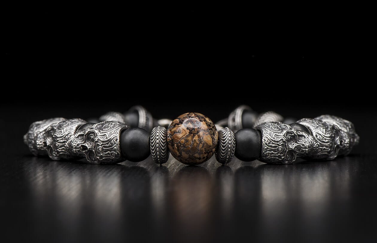 Silver and black beaded bracelet with ornate skull beads, textured spacers, and a central brown marbled stone bead.