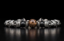 Silver and black beaded bracelet with ornate skull beads, textured spacers, and a central brown marbled stone bead.
