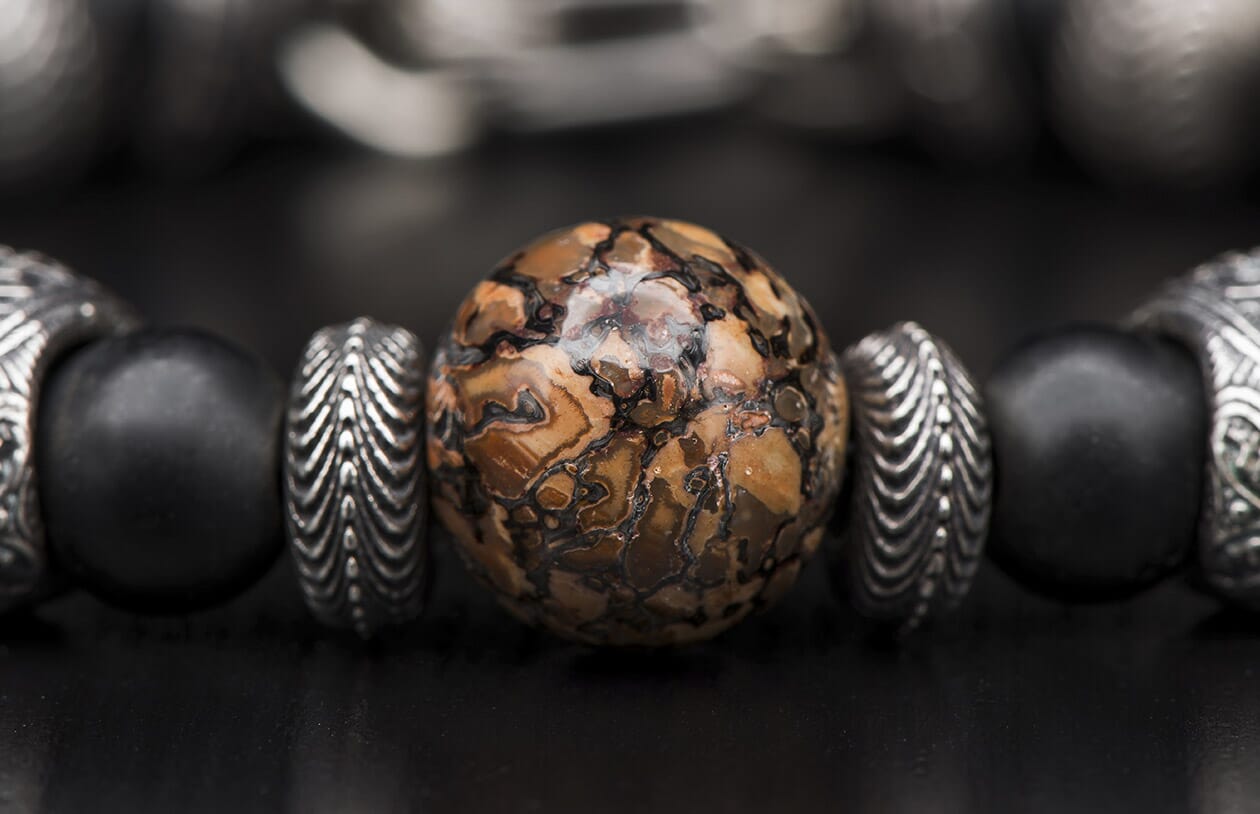Beaded bracelet with a central brown and black patterned stone bead, flanked by ribbed silver and matte black beads.