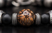 Beaded bracelet with a central brown and black patterned stone bead, flanked by ribbed silver and matte black beads.