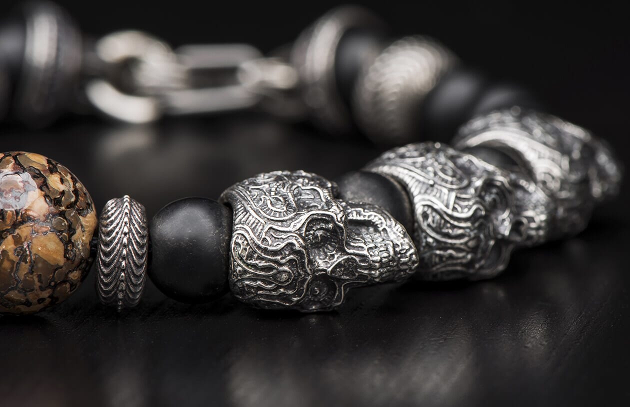 Ornate silver skull and bead bracelet with black matte beads and a brown marbled bead.