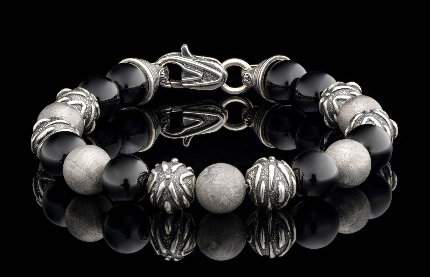 Bracelet with polished black onyx and detailed silver beads, some featuring a meteoritic pattern, connected by an ornate silver clasp.