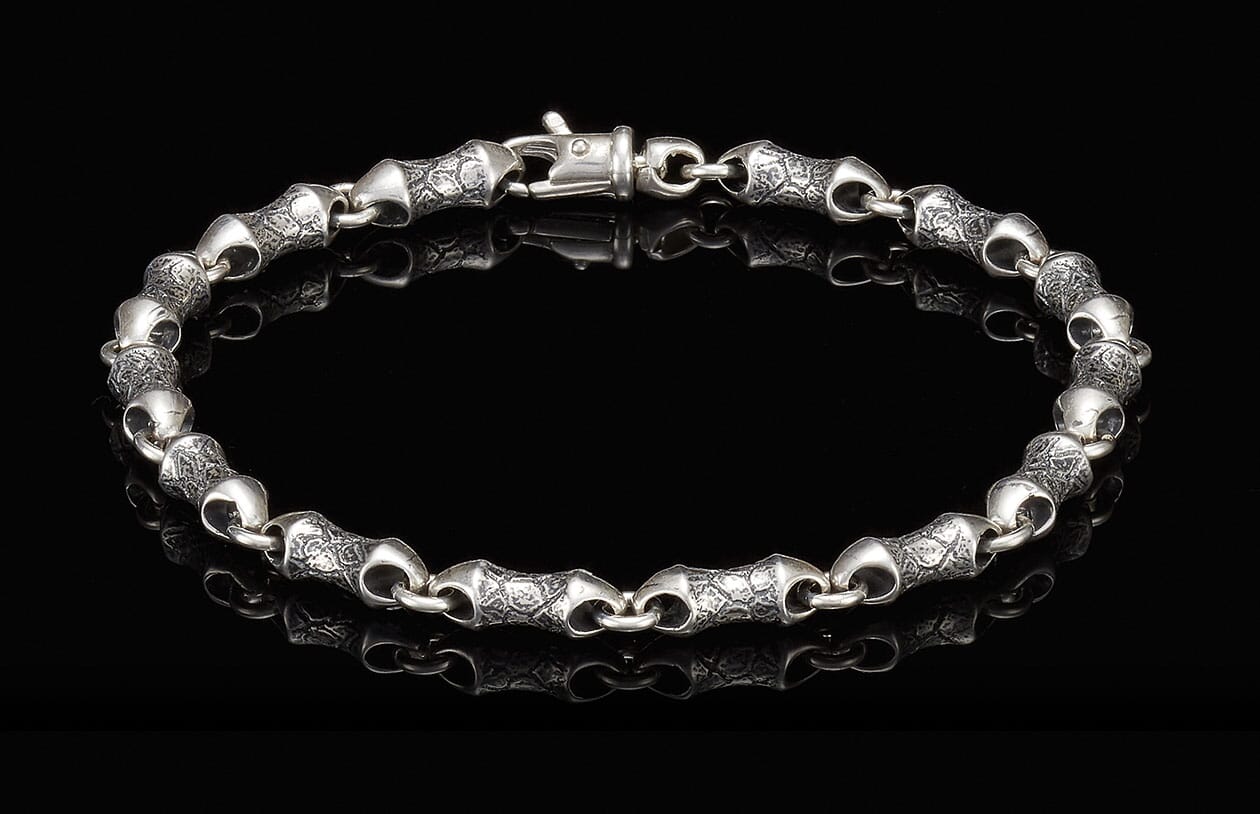 Oxidized silver bracelet with textured, barrel-shaped links and a lobster clasp, reflected on black.