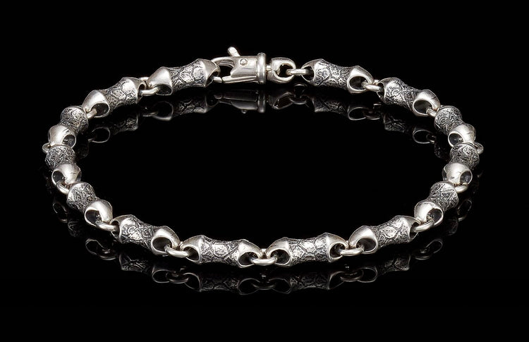 Oxidized silver bracelet with textured, barrel-shaped links and a lobster clasp, reflected on black.
