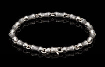 Silver bracelet with textured, barrel-shaped links and a decorative clasp on a reflective black surface.