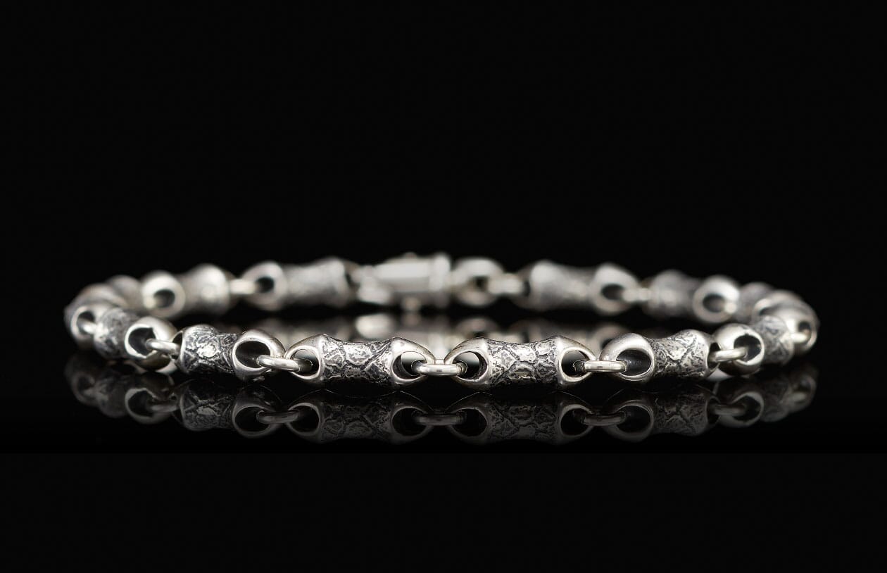 Silver chain bracelet with textured, irregular links and a visible clasp on a reflective black surface.