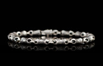 Silver chain bracelet with textured, irregular links and a visible clasp on a reflective black surface.