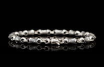 Silver metal bracelet with textured, intricately engraved links and a hook clasp, reflecting on black.