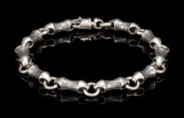 Textured silver bracelet featuring stylized, elongated links with an engraved pattern and a toggle clasp, laid flat.