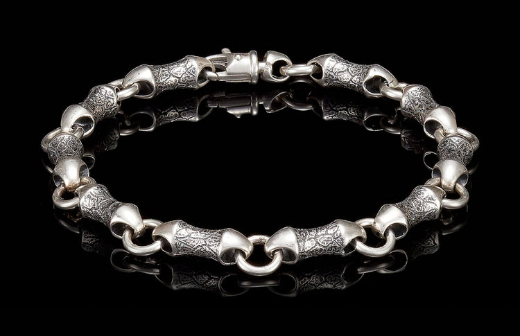 Textured silver bracelet featuring stylized, elongated links with an engraved pattern and a toggle clasp, laid flat.
