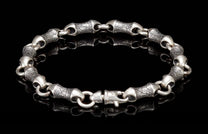 Silver-toned metal bracelet with textured, bamboo-shaped links and a lobster clasp, reflecting on a black surface.