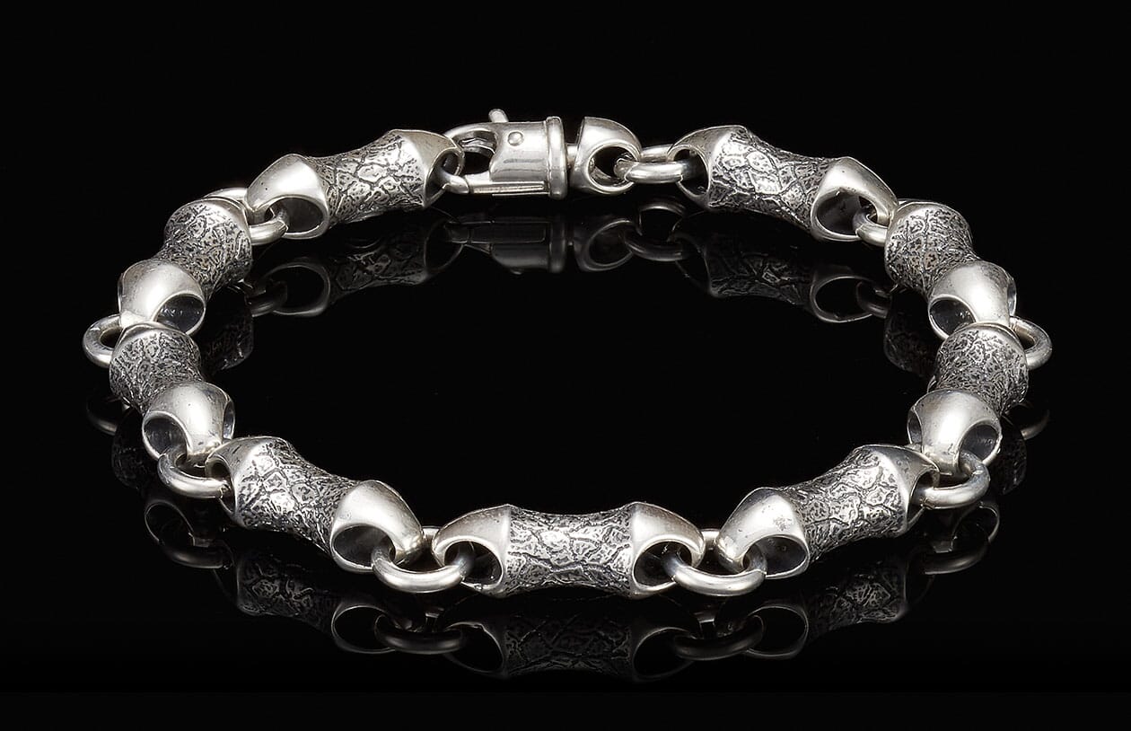 Silver-toned metal bracelet with textured cylindrical links, smooth connecting rings, and a prominent box clasp.