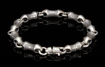 Silver bracelet with textured, scale-like links and a lobster clasp on a reflective black surface.