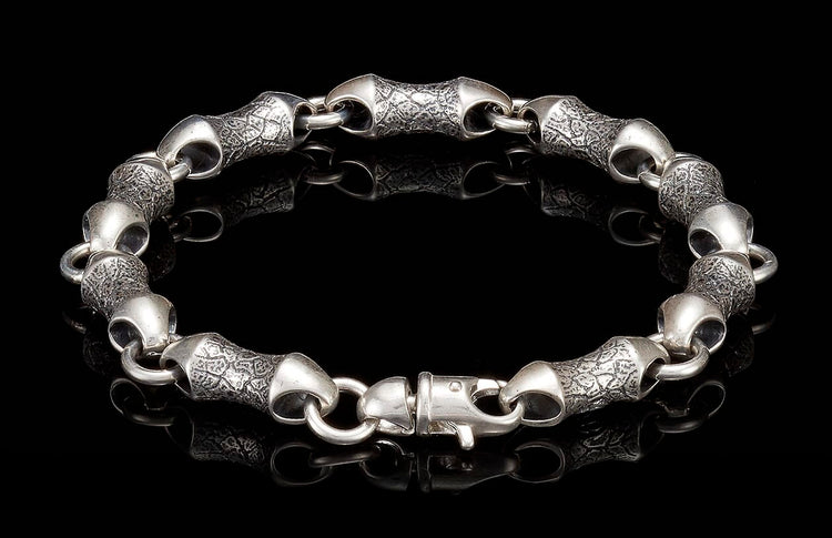 Silver bracelet with textured, scale-like links and a lobster clasp on a reflective black surface.
