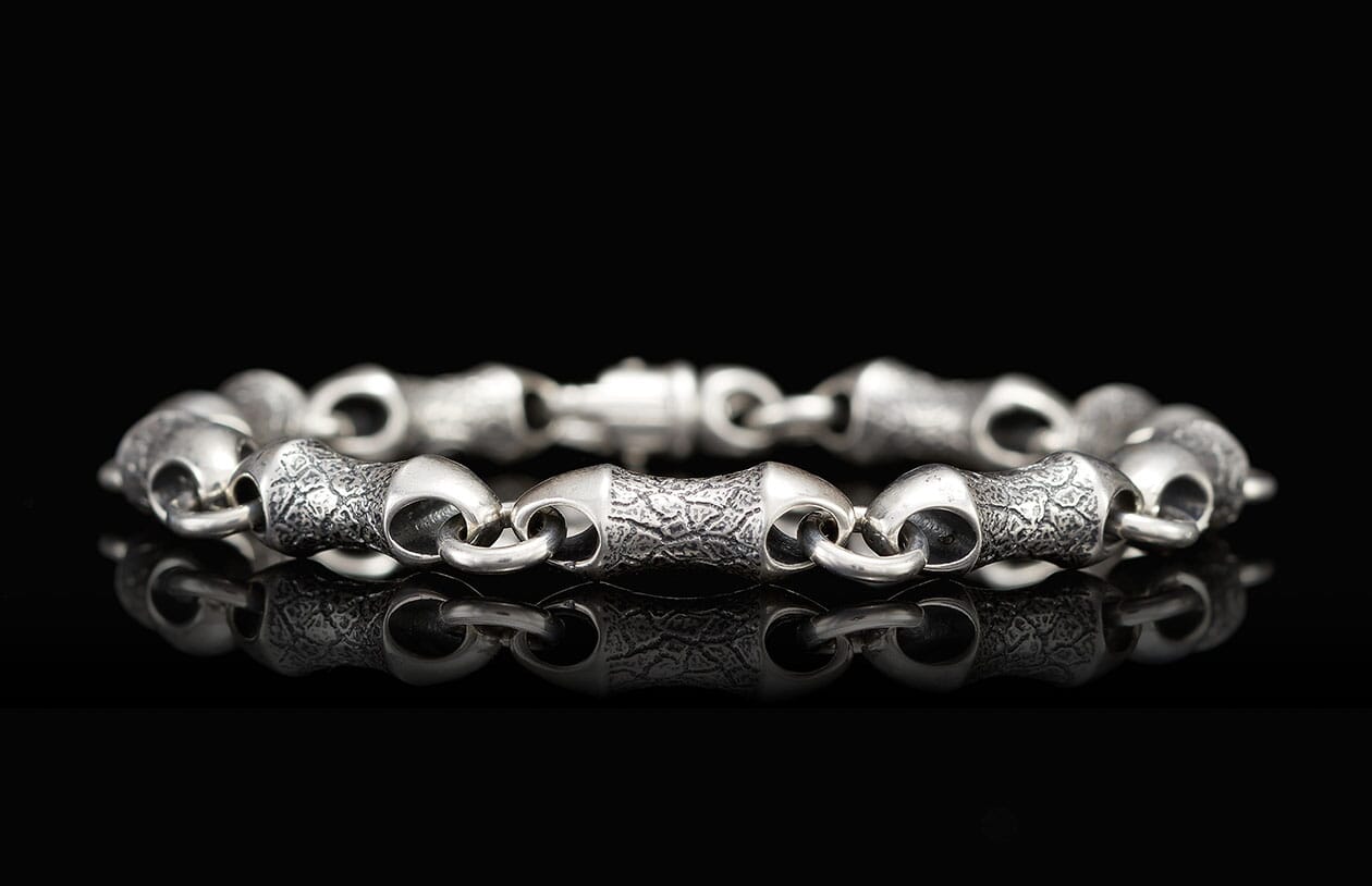 Chunky silver bracelet with alternating textured and smooth barrel-shaped links, on a reflective black surface.