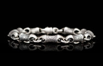 Chunky silver bracelet with alternating textured and smooth barrel-shaped links, on a reflective black surface.