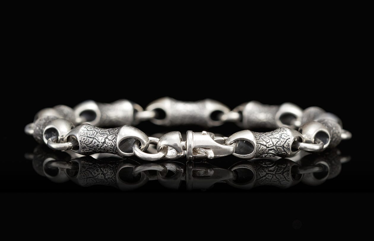 Textured silver bracelet with distinct links and a lobster clasp, reflecting on black.