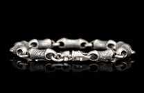Textured silver bracelet with distinct links and a lobster clasp, reflecting on black.