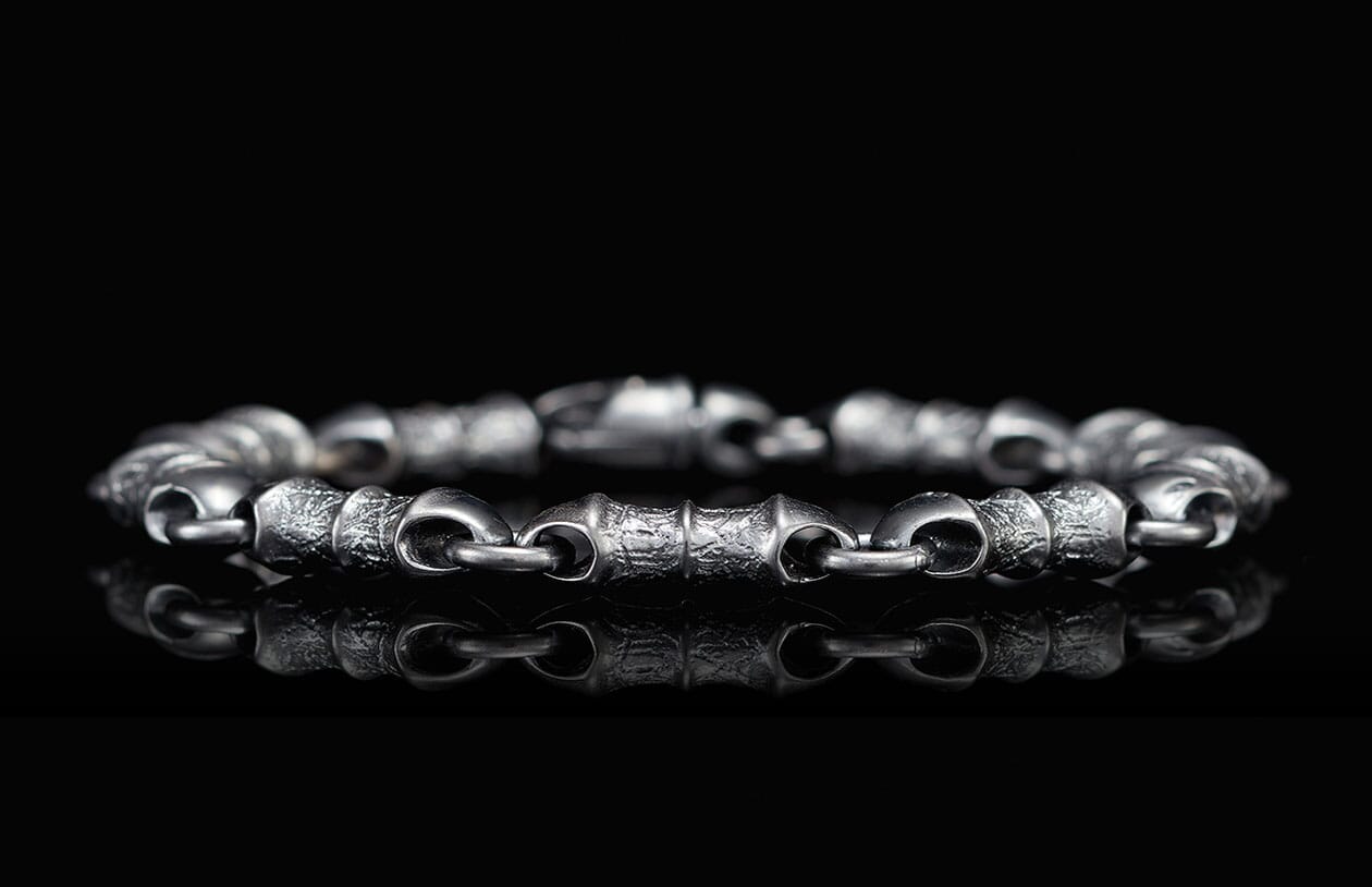 Textured dark silver-toned linked bracelet reflecting on a glossy black surface.